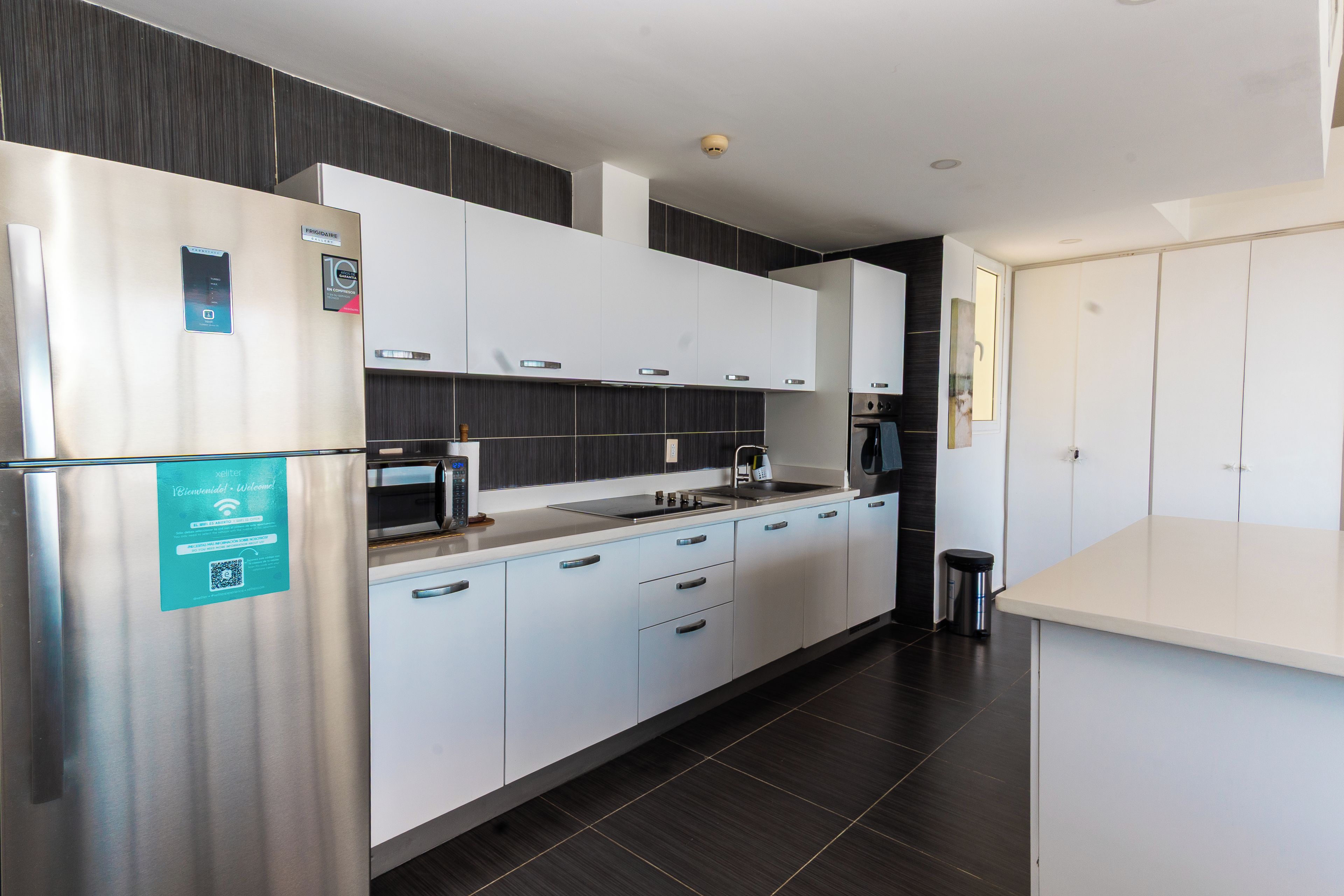 Een moderne keuken met roestvrijstalen apparatuur, witte kasten en donkere vloer.