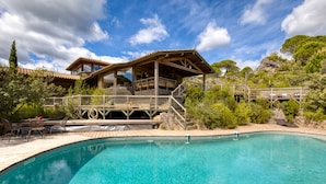 A pool with a wooden deck and a building with a balcony overlooking it. - Family Villa in Exceptional Setting with Mountain View, Wi-Fi, and Air Conditioning (Mourèze)