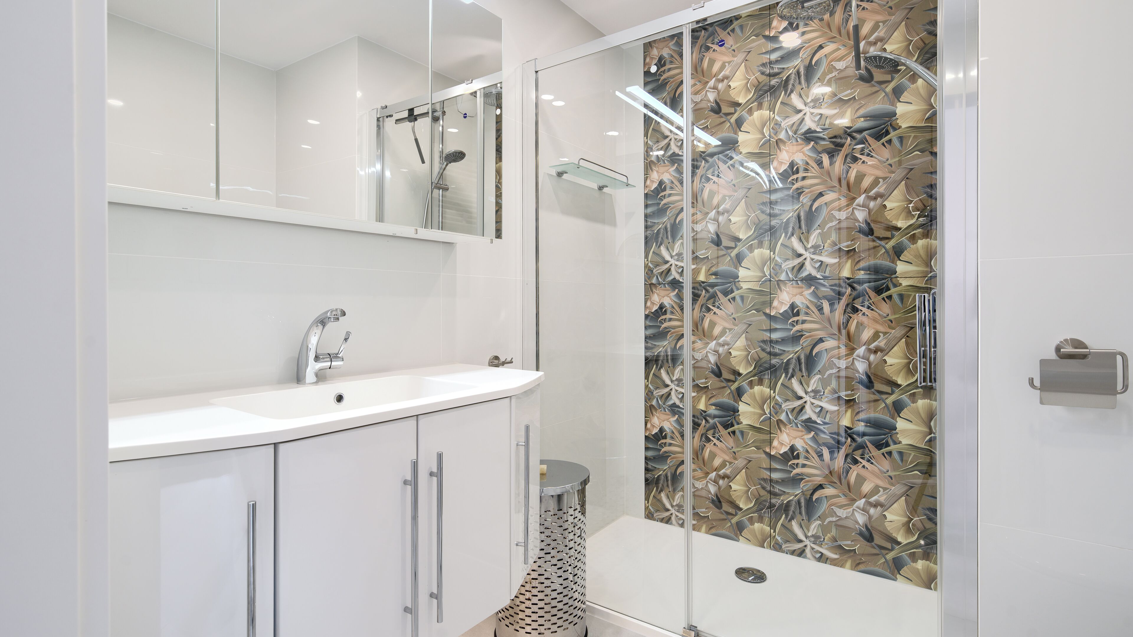 A modern bathroom with a glass shower enclosure, a white sink, and a mirror above it.