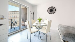 A modern apartment with a glass dining table set for four, white chairs, a grey sofa, and a black wall clock. - Sun & Snow Odrzanskie Bulvary (Szczecin)
