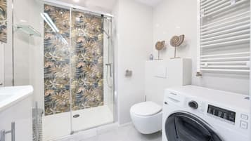 Une salle de bain moderne avec une douche à parois de verre, des toilettes et un lave-linge à chargement frontal.