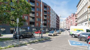 Une rue bordée de voitures garées, un fourgon jaune et des immeubles à plusieurs étages dotés de balcons.