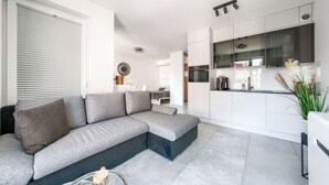 A modern living room with a grey sectional sofa, a dining area with a table and chairs, and a kitchen with white cabinets and a black countertop. - Sun & Snow Odrzanskie Bulvary (Szczecin)