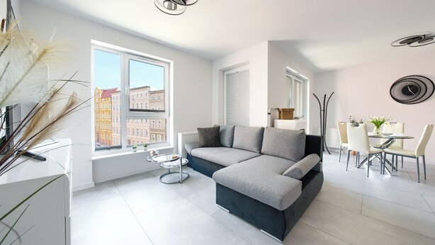 A modern living room with a grey sectional sofa, a dining table with chairs, and large windows offering a view of buildings. - Sun & Snow Odrzanskie Bulvary (Szczecin)