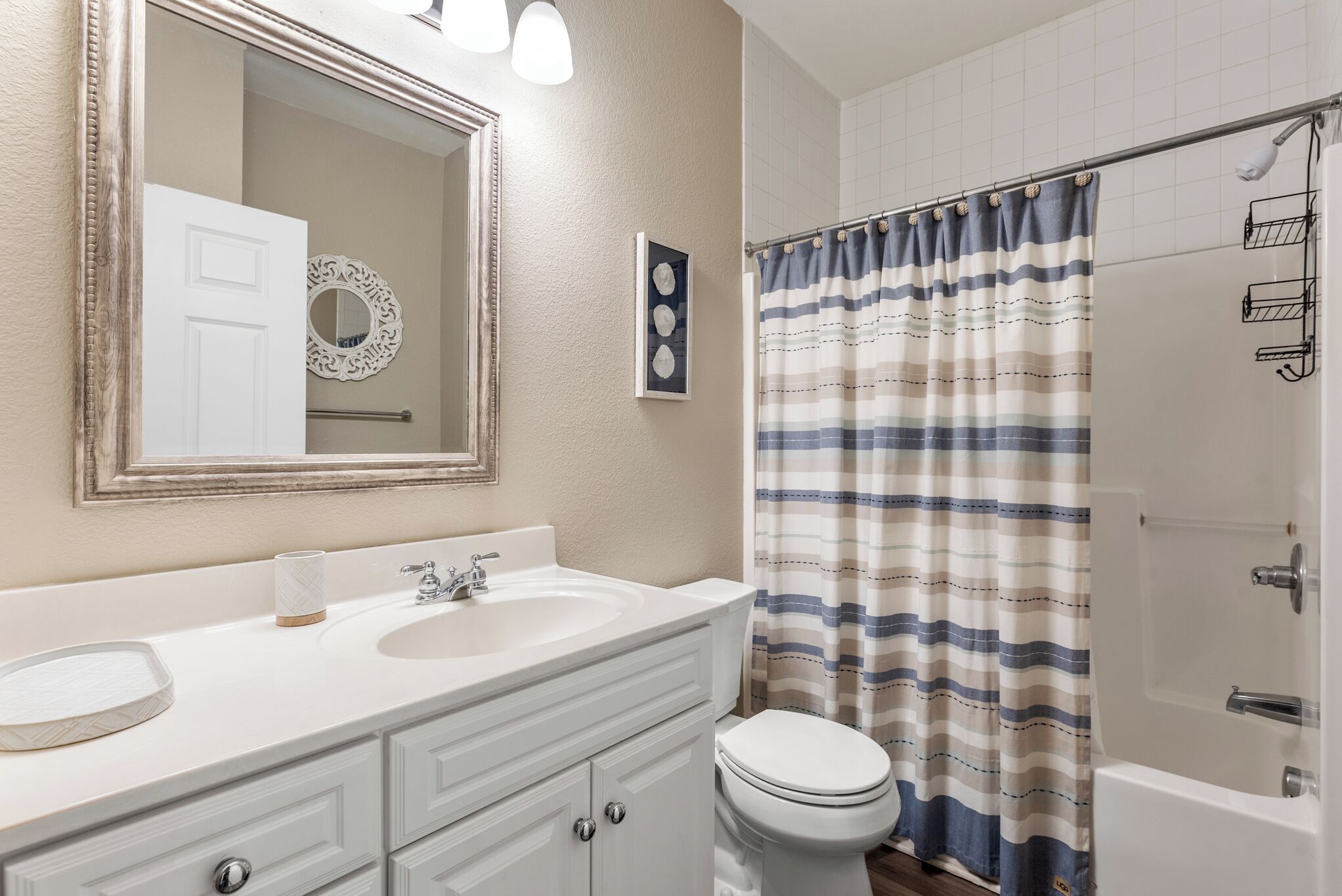A bathroom with a white vanity, two sinks, a toilet, and a shower with a striped curtain.