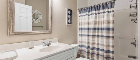 A bathroom with a white vanity, two sinks, a toilet, and a shower with a striped curtain.