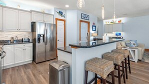Une cuisine moderne avec des meubles blancs, des appareils en acier inoxydable et un îlot central doté de tabourets de bar.