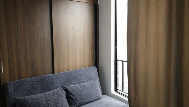 Ein Zimmer mit einer Couch, einem Vorhangfenster und Holzschränken.