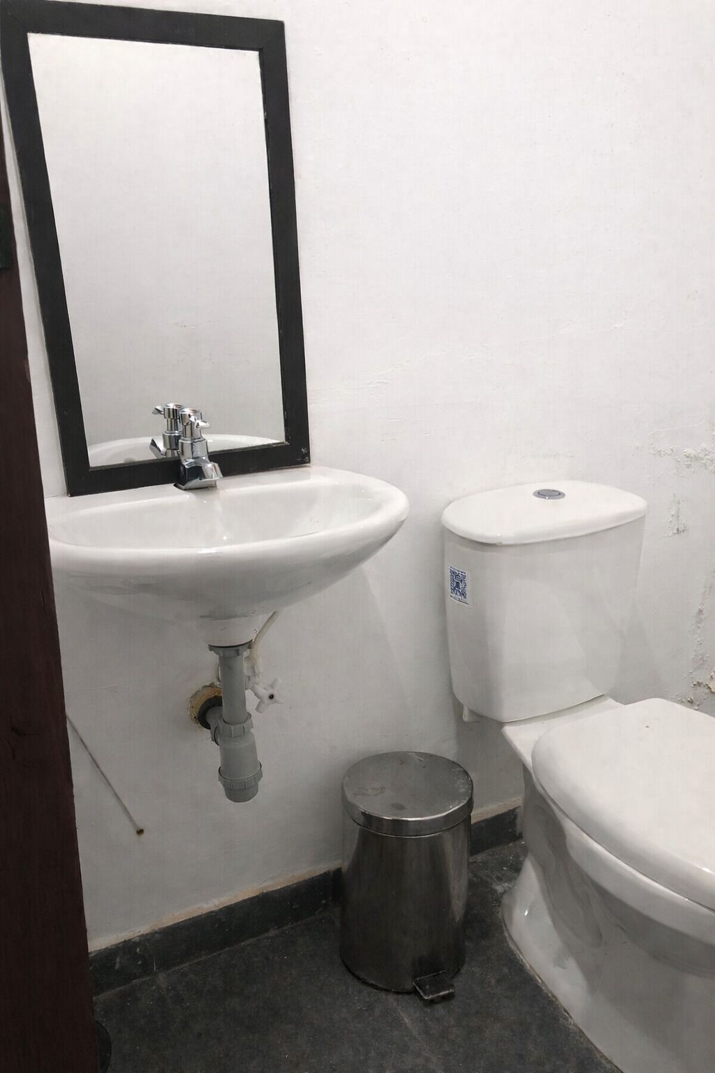 Een badkamer met een witte wastafel, een spiegel, een toilet en een prullenbak.
