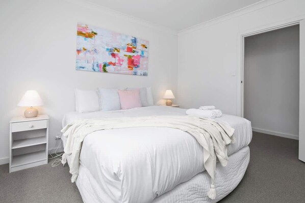 Ein Schlafzimmer mit einem Bett, zwei Nachttischen, einem an der Wand befestigten abstrakten Gemälde und einer Tür.