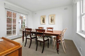 A dining room with a wooden table and chairs, a white door, and two framed pictures on the wall.