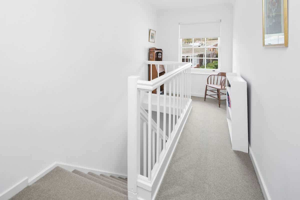 A narrow staircase with white railings leading to a landing. A wooden clock and a framed picture are visible on the landing wall.