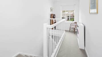 A narrow staircase with white railings leading to a landing. A wooden clock and a framed picture are visible on the landing wall.