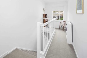 A narrow staircase with white railings leading to a landing. A wooden clock and a framed picture are visible on the landing wall. - Between City & Hills (Mitcham)