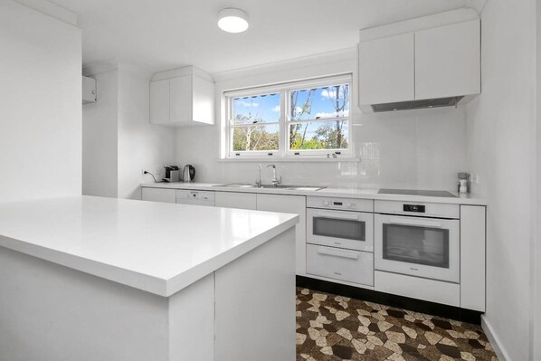 A modern kitchen with white cabinetry, a large island, a window, and a tiled backsplash.