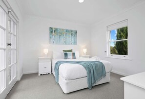 A bedroom with a bed, bedside tables, a window, and a painting on the wall.