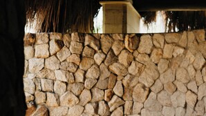 Una bañera grande, blanca y ovalada en un entorno rústico, con un muro de piedra y suelo de madera.