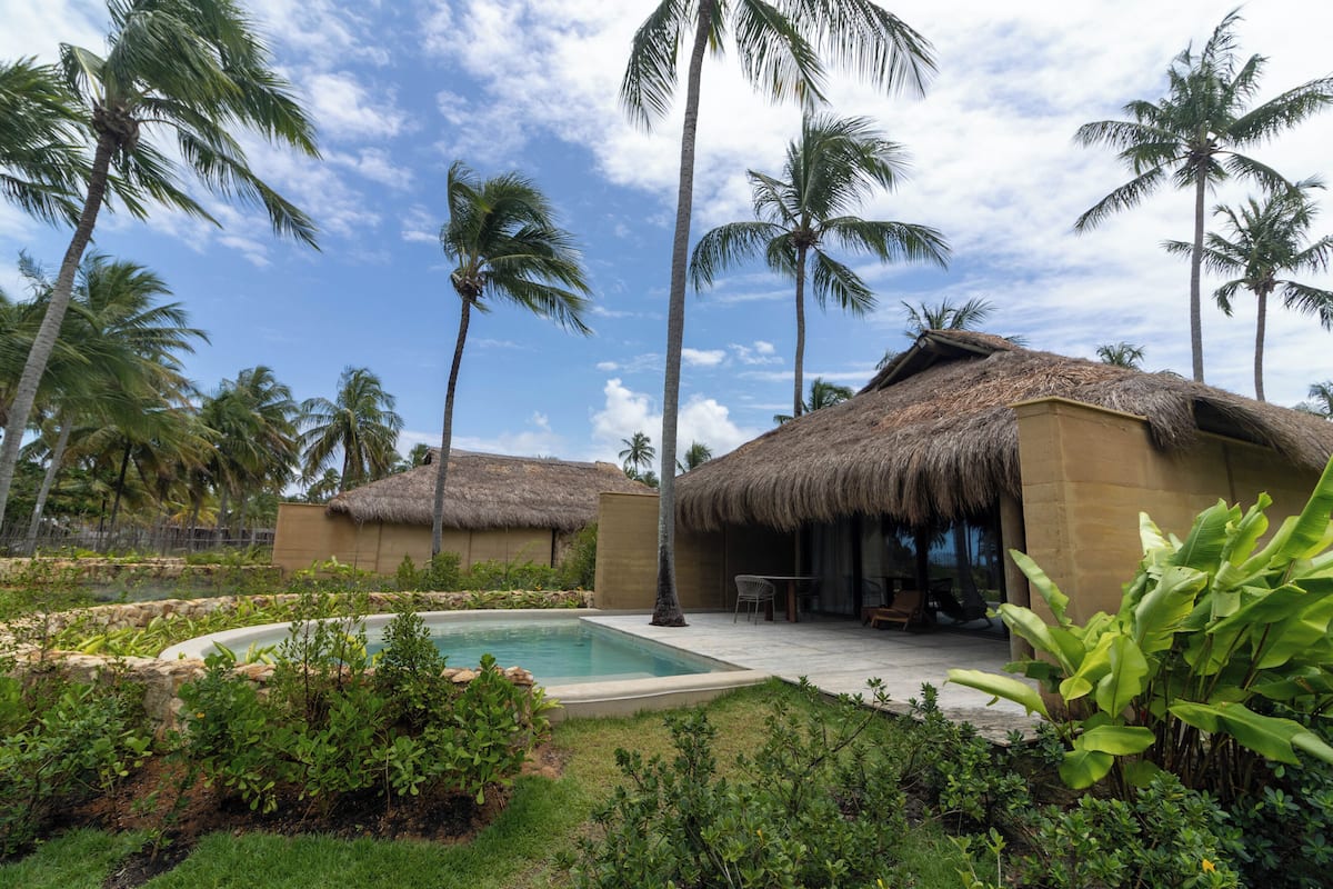 Un resort con cabañas de techo de paja, una piscina y abundante vegetación.