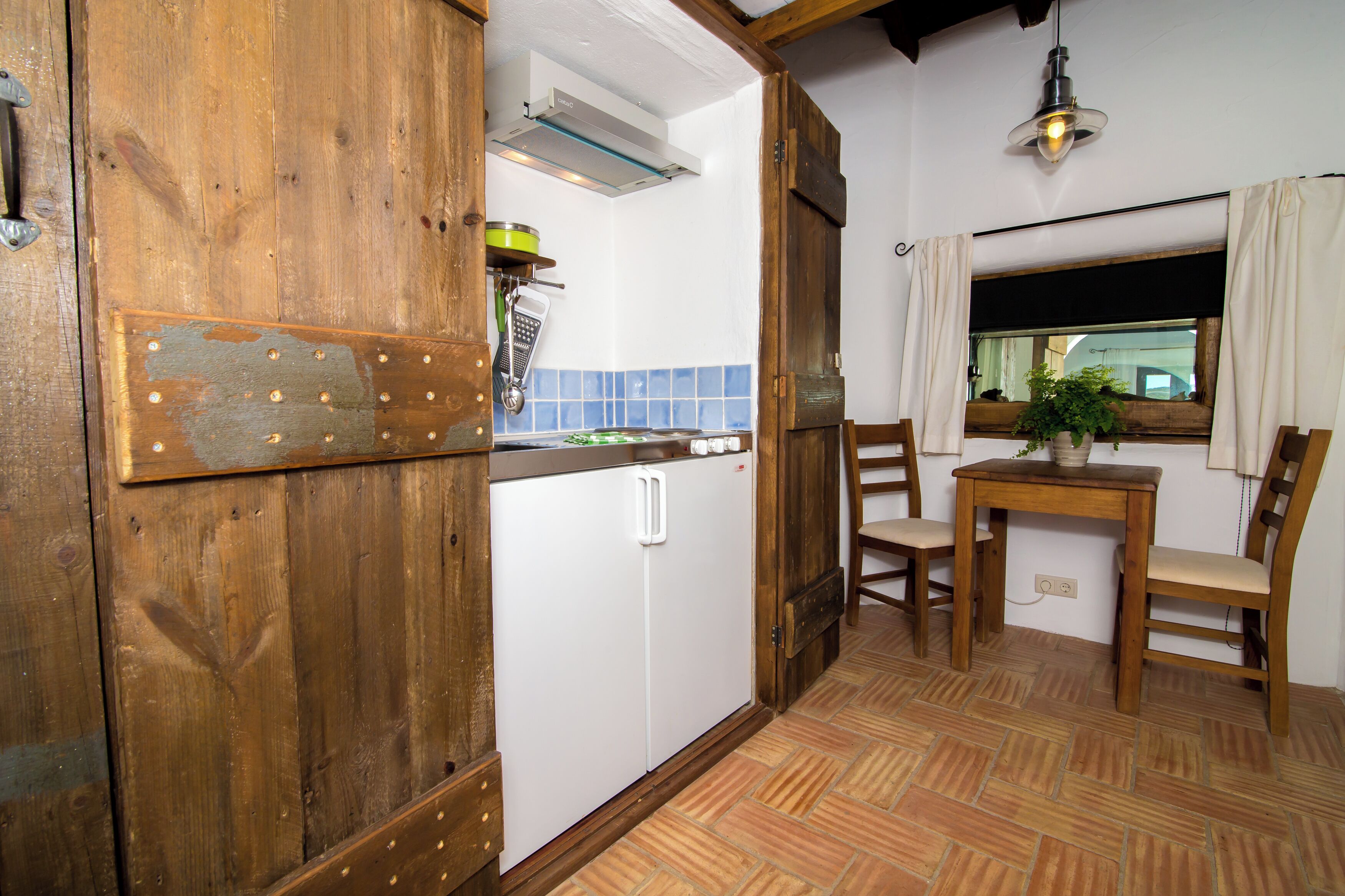 Eine kleine Küche mit Holztür, weißem Kühlschrank und einem Essbereich mit zwei Stühlen und einem Tisch.
