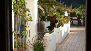 Eine Terrasse im Freien mit einer weißen Wand, Pflanzkübeln und einer Sitzgruppe mit Stühlen.