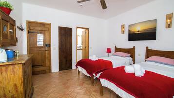 Una habitación con dos camas, un escritorio de madera, un ventilador de techo y un cuadro de un atardecer.
