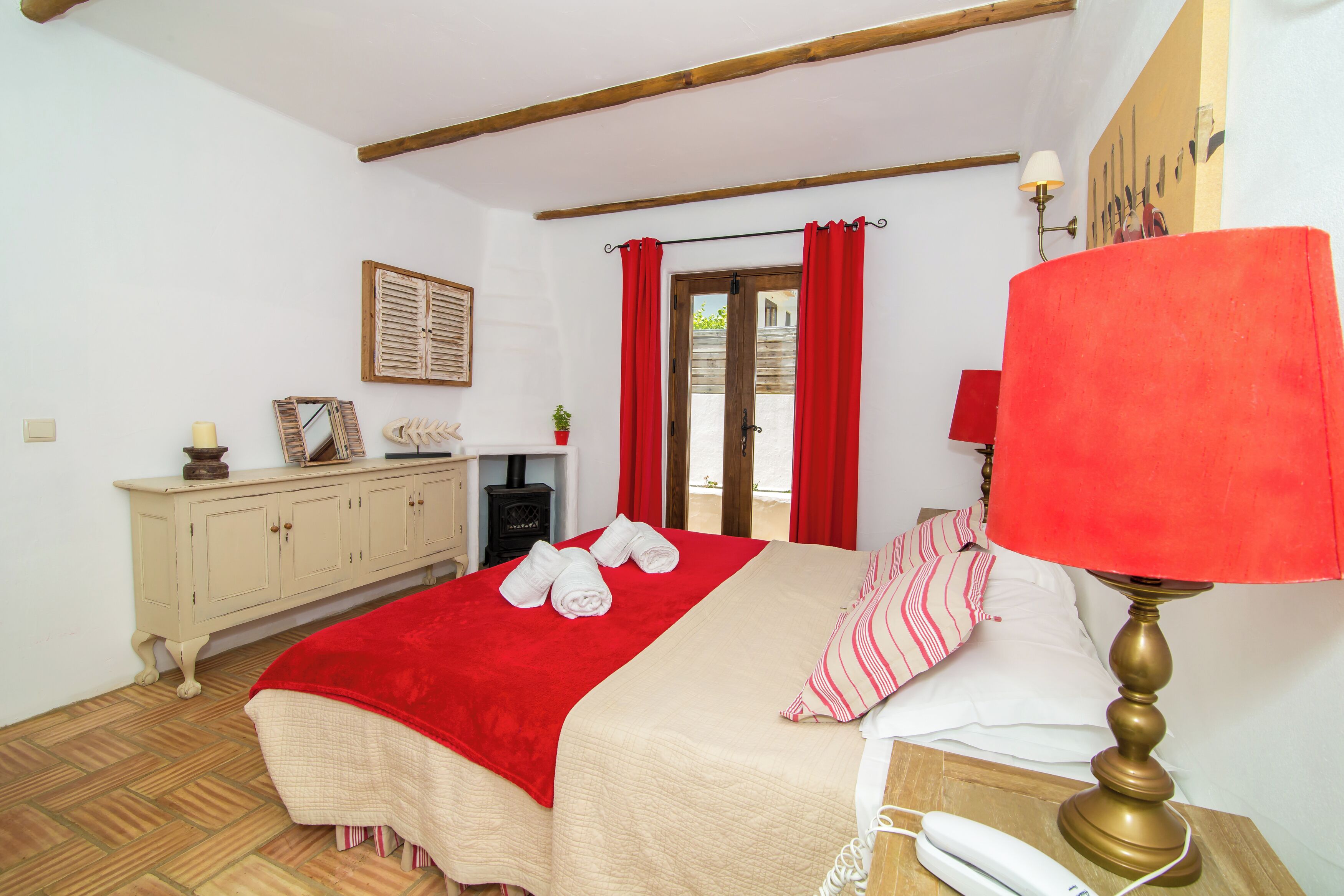 Une chambre à coucher avec un lit, une lampe de chevet, une commode et une fenêtre avec des rideaux.