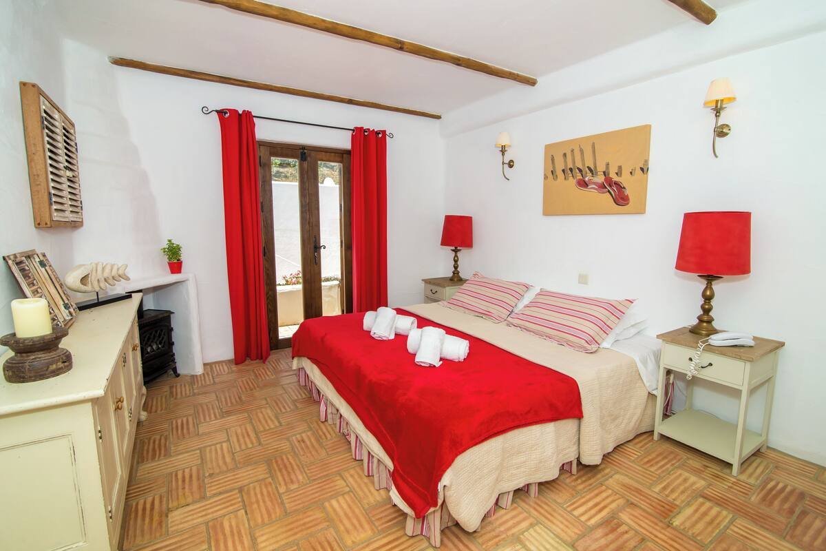 A bedroom with a bed, bedside tables, a lamp, a painting, and a window with curtains.
