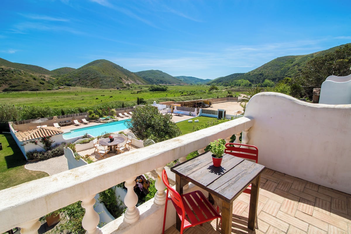 A balcony with a view of a swimming pool, surrounded by lush greenery and hills.