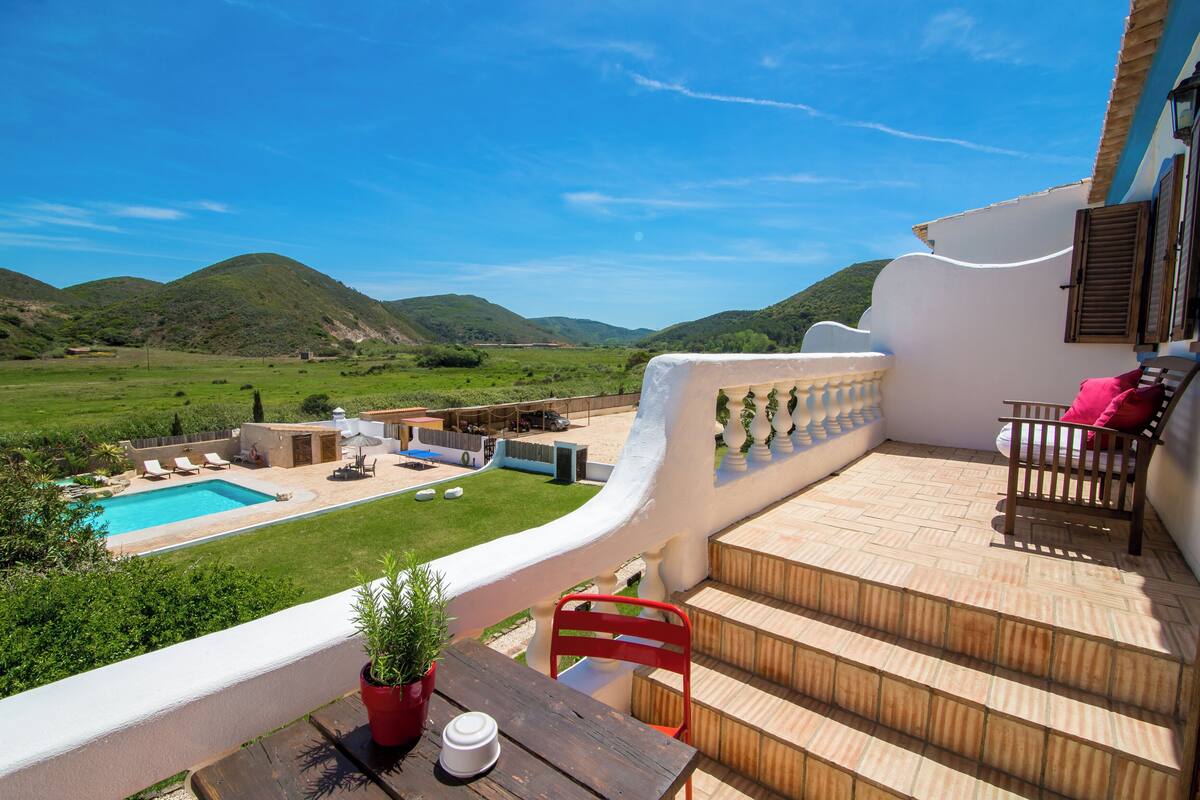 A terrace with a pool, outdoor seating, and a view of green hills.