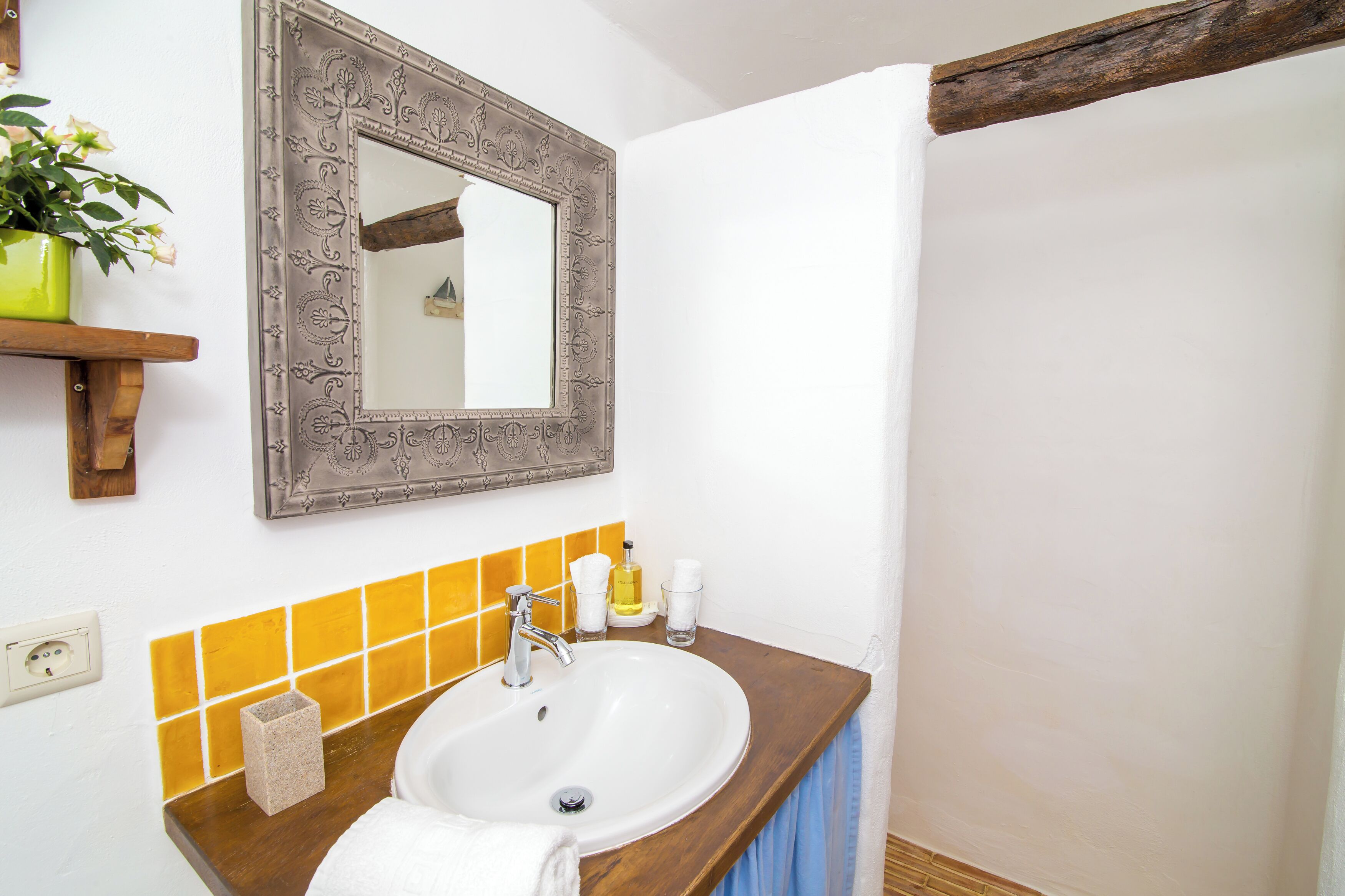 Une salle de bain avec un lavabo blanc, un miroir doté d’un cadre orné et un pare-feu en carreaux jaunes.