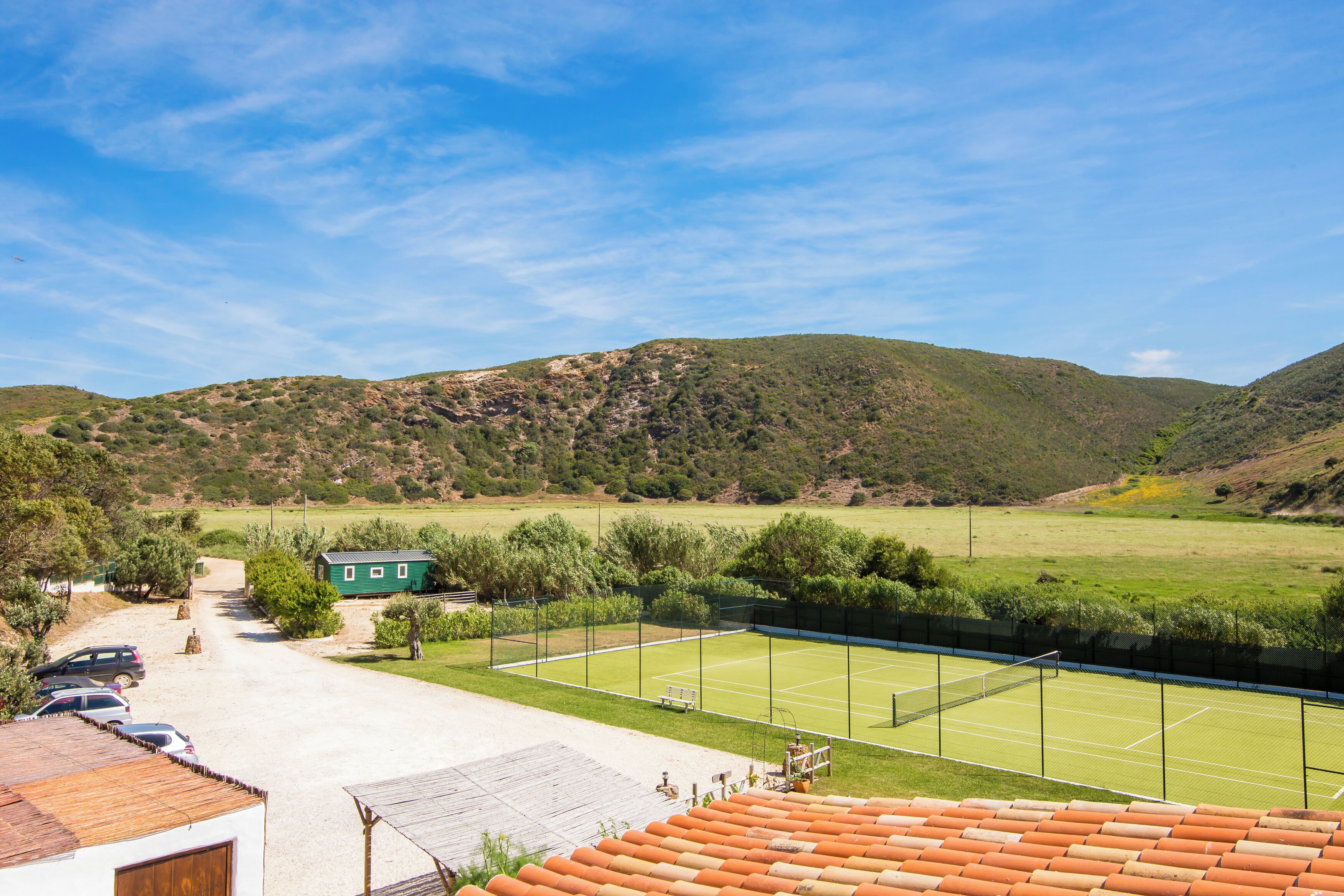 Un court de tennis avec un filet, entouré d’une clôture, et un bâtiment avec un toit végétalisé en premier plan.