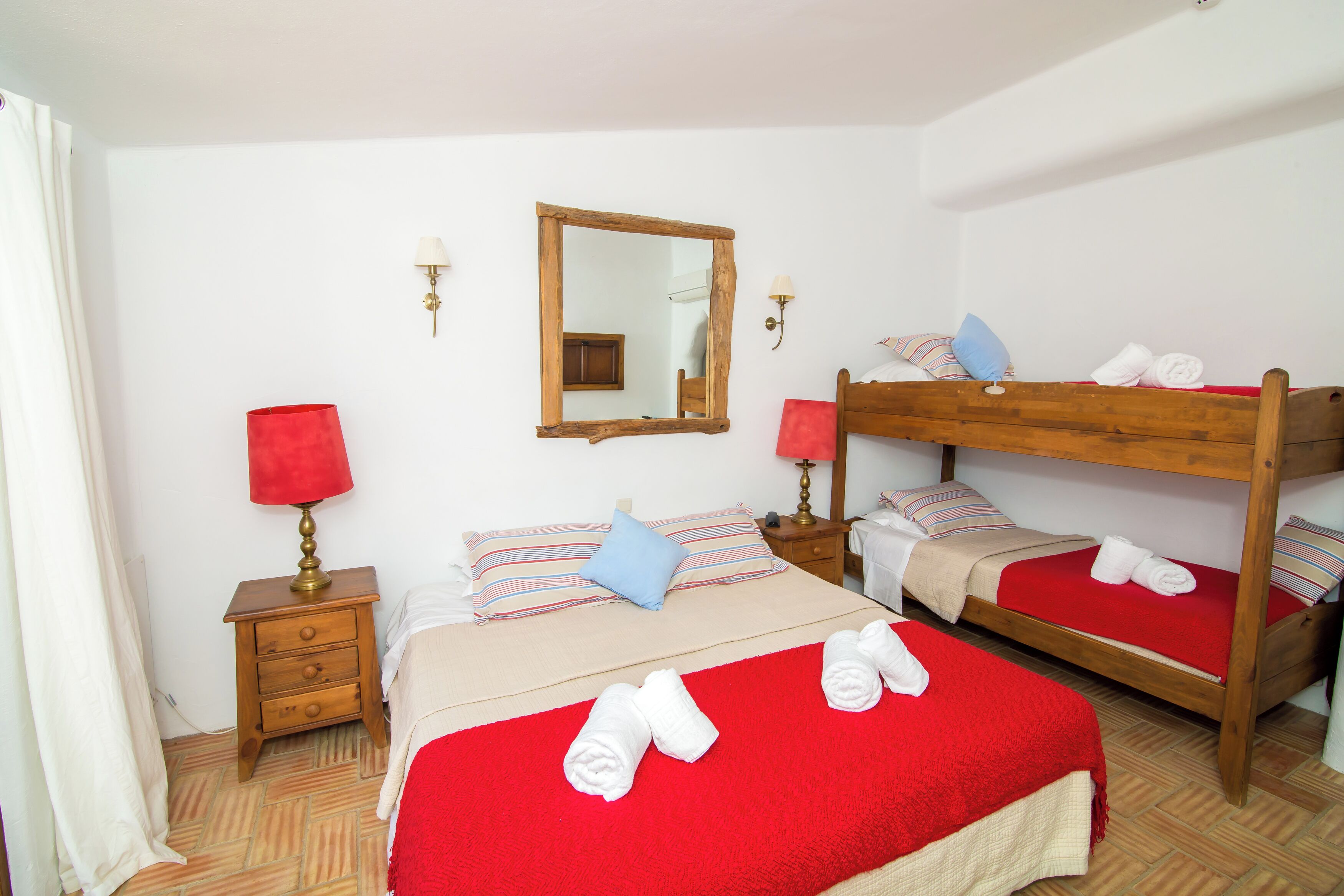 A room with two bunk beds, a wooden nightstand with a lamp, a mirror, and a red blanket on the floor.