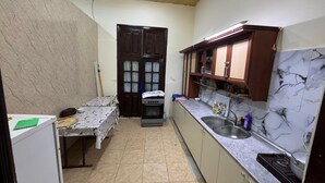 A compact kitchen with a tiled floor, a stove, a sink, and wooden cabinets. - Gulf Hostel (Baku)