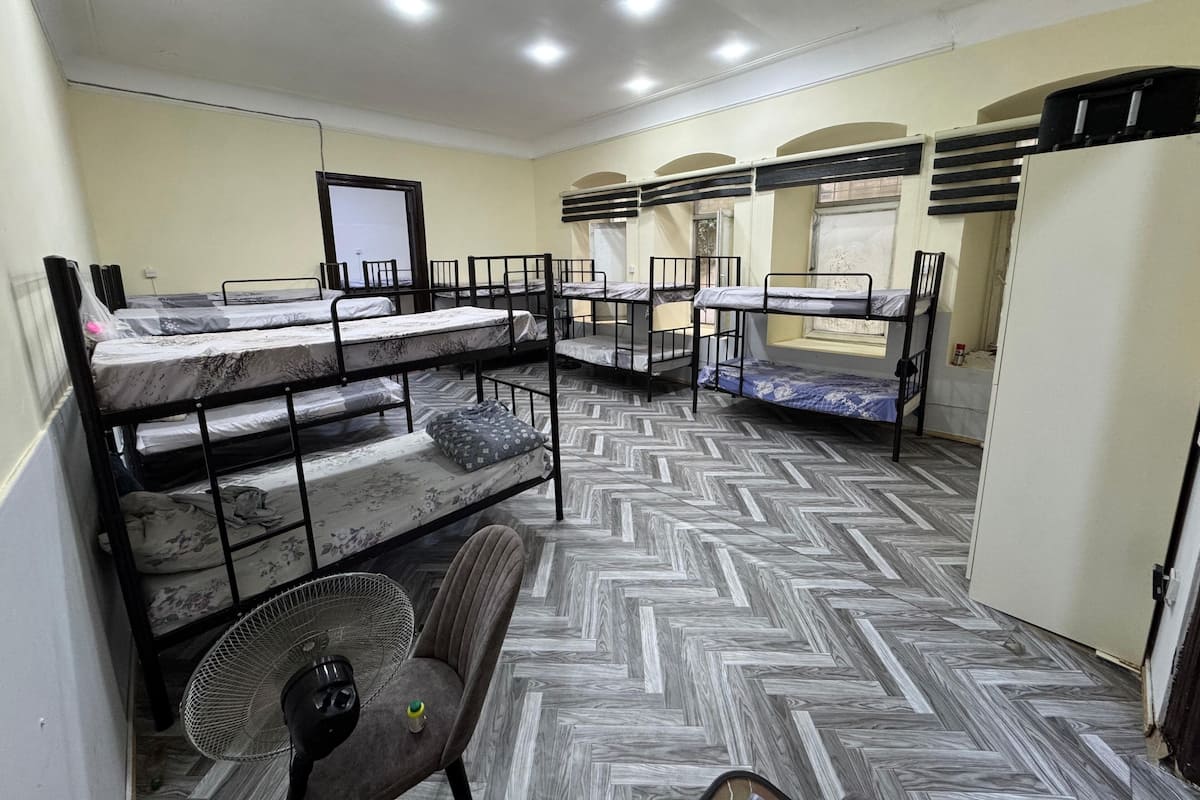 A dormitory room with bunk beds, a fan, and a window.