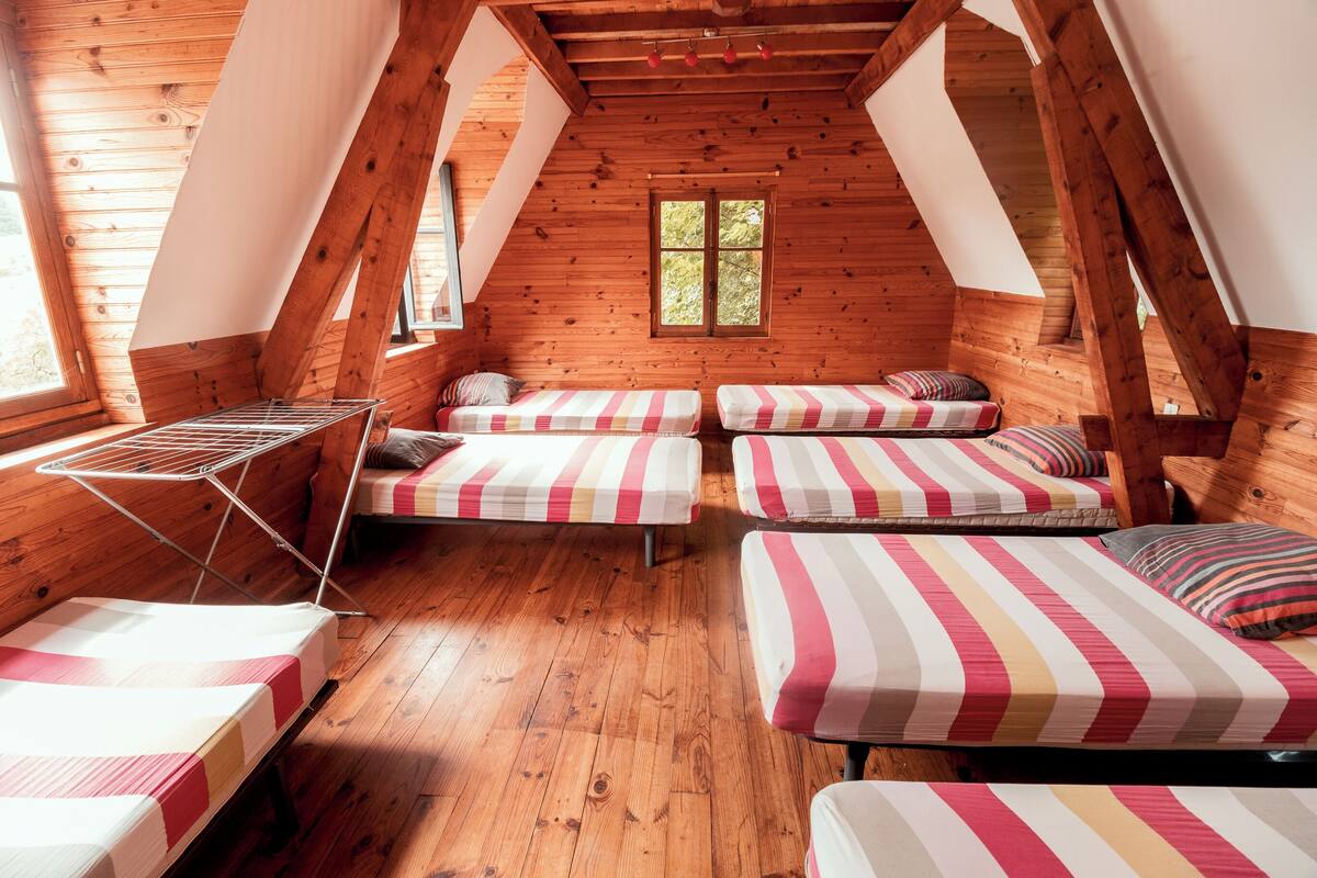 A cozy attic bedroom with wooden walls and sloped ceilings, featuring four beds with striped bedding and a drying rack.