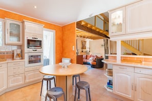 A modern kitchen with built-in appliances, a dining area with stools, and a staircase leading to an upper level. - Villa 'Le Verger Du Midi' with Shared Pool, Private Terrace and Wi-Fi (Cadenet)