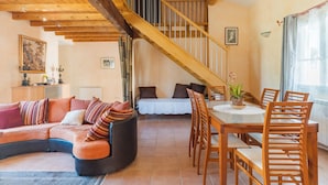 A cozy living room with a curved sofa, a dining table with chairs, a staircase, and a view of the outdoors. - Villa 'Le Verger Du Midi' with pool, private terrace, and Wi-Fi (Cadenet)