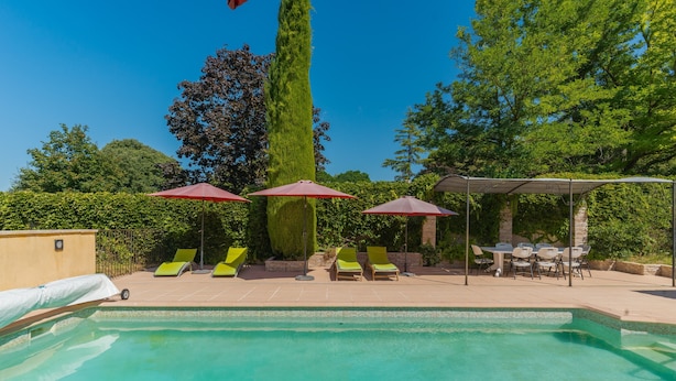 A swimming pool with lounge chairs and umbrellas, surrounded by trees and a brick wall. - Villa 'Le Verger Du Midi' with pool, private terrace, and Wi-Fi (Cadenet)