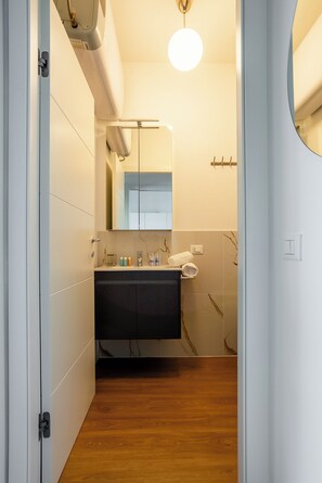 A modern bathroom with a wooden floor, a dark vanity, a mirror, and a towel rack.