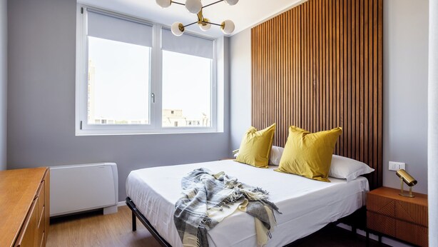 Ein Schlafzimmer mit einem Bett, einem Nachttisch, einer Lampe, einem Fenster und einer Heizung.