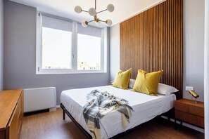 A bedroom with a bed, a nightstand, a lamp, a window, and a radiator.
