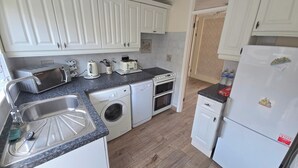 A compact kitchen with white cabinets, a washing machine, a toaster, and a refrigerator. - Herne Bay - House - Sleeps 7 - Parking (Herne Bay)