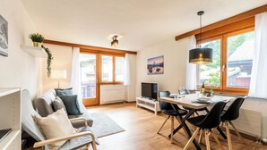 Una sala de estar moderna con un sofá, una mesa de comedor y sillas, un televisor y una ventana con cortinas.