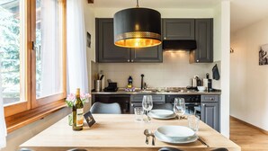 Una cocina moderna con armarios oscuros, una mesa de comedor de madera para dos personas y una lámpara colgante.