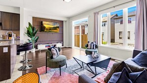 Een moderne woonkamer met keuken, grote ramen en uitzicht op omliggende huizen.