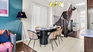Een eetruimte met een ronde tafel, stoelen, een lamp en een trap naar een ander niveau.