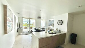 A modern kitchen with a large island, a dining area with a sofa, and a view of the cityscape through large windows.