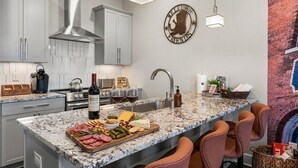 A modern kitchen with granite countertops, stainless steel appliances, and a central island with a wine bottle and charcuterie board.