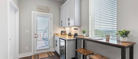 A modern kitchen with a built-in oven, a coffee station, and a view through the window.