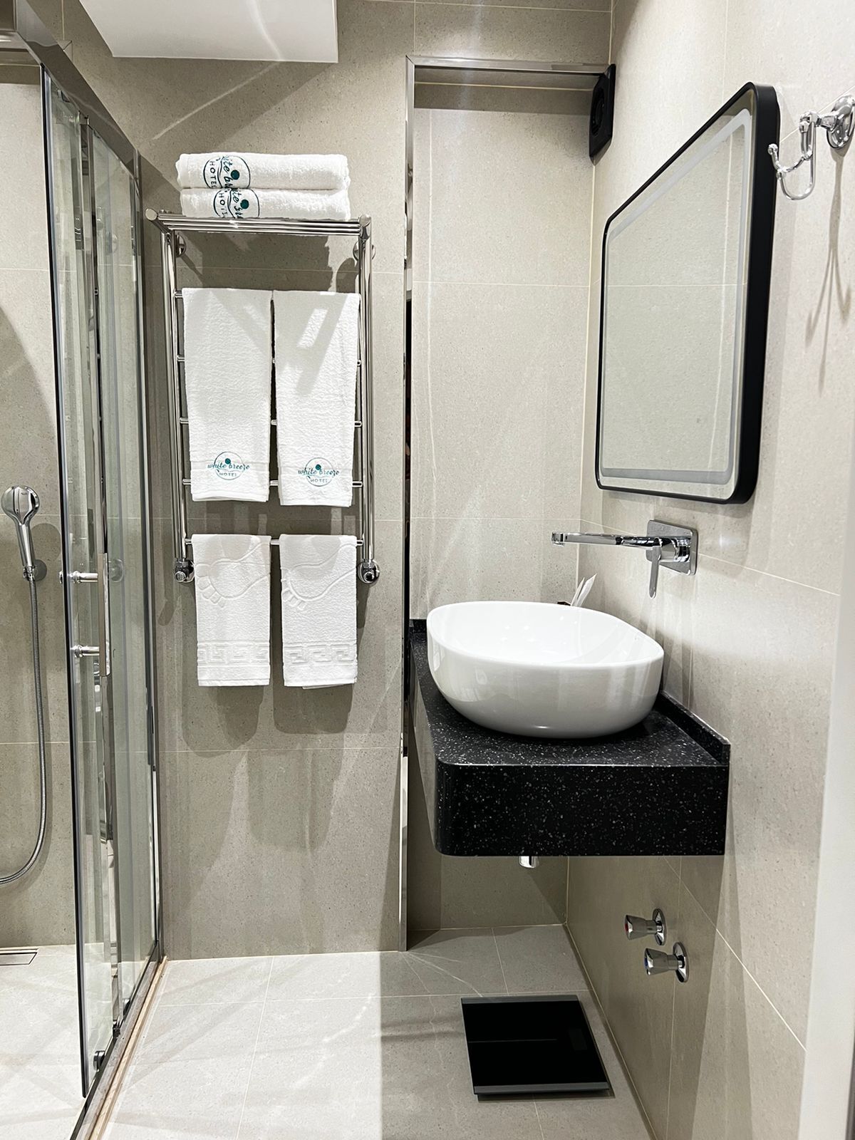 A modern bathroom with a glass shower enclosure, a white sink with a black countertop, and a mirror above the sink.